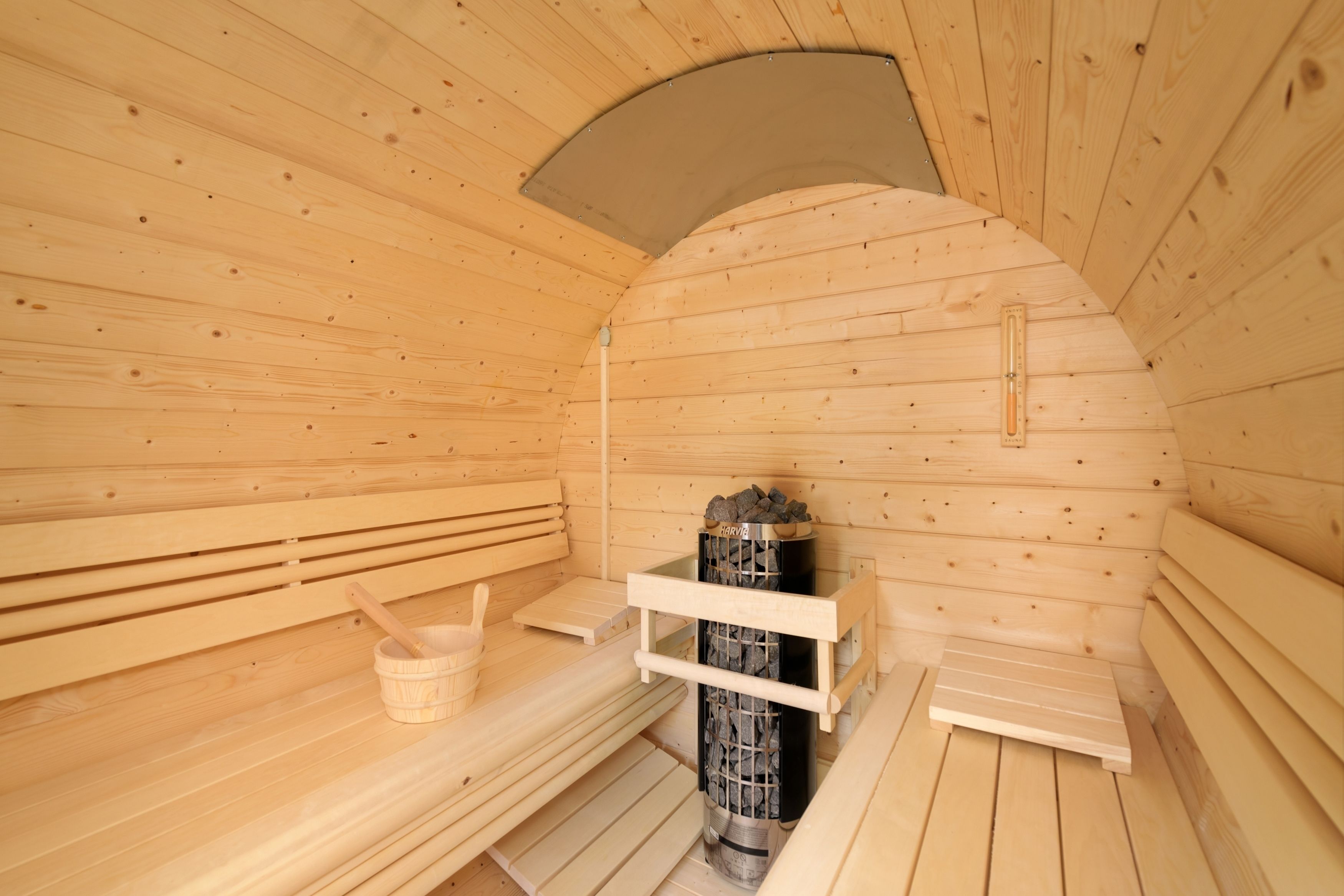 Una sauna in legno con panche, un catino di legno e uno scaffale in pietra.