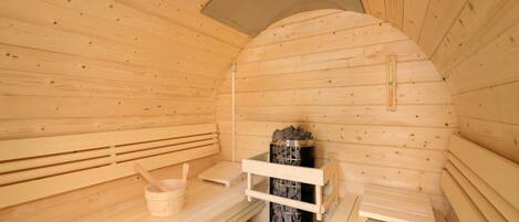 Una sauna in legno con panche, un catino di legno e uno scaffale in pietra.