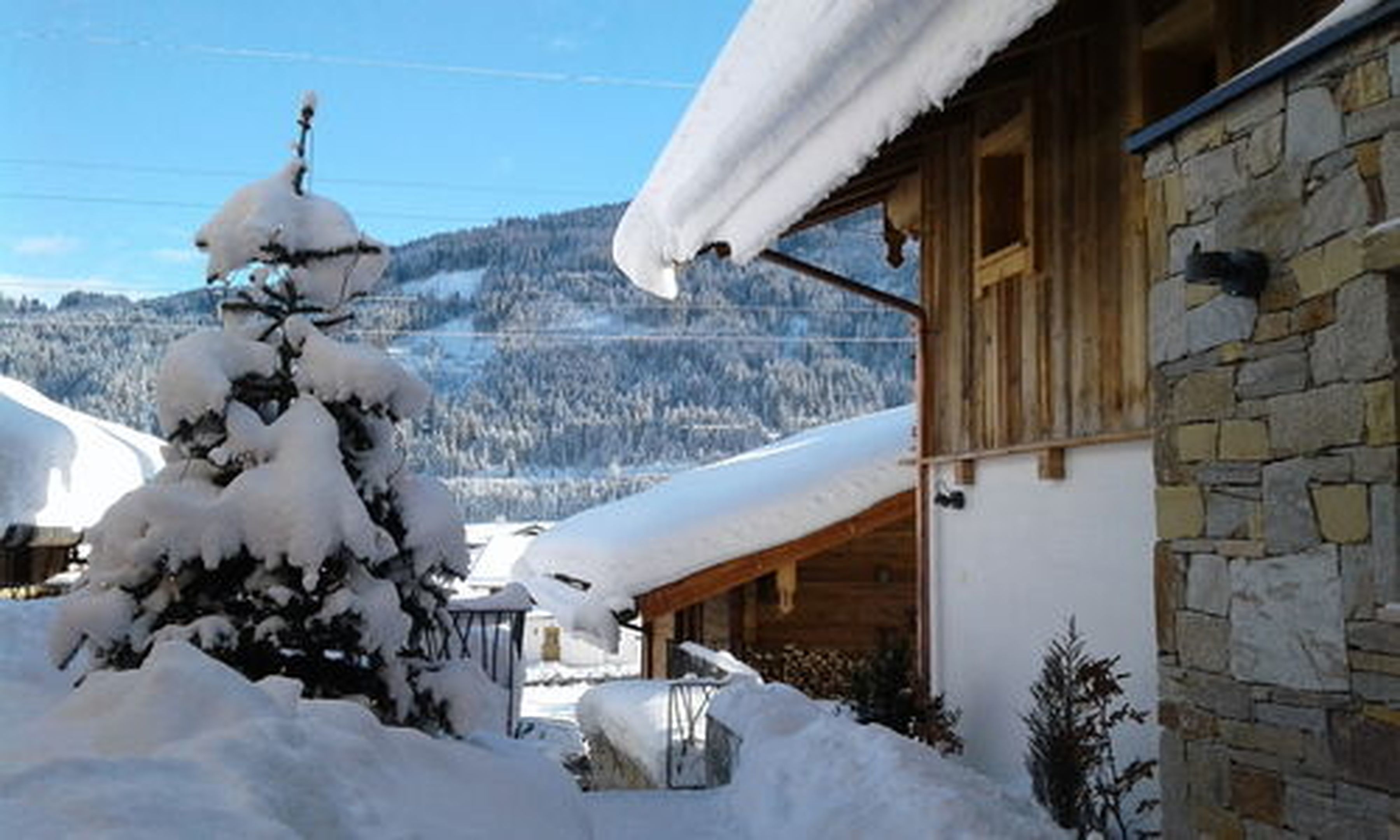 Eine verschneite Berglandschaft mit einer Holzhütte, die Steinmauern und ein geneigtes Dach hat.