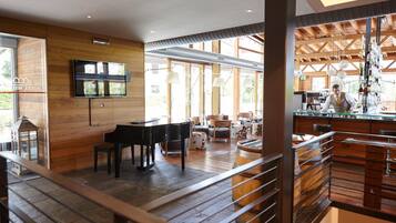 Ein modernes Hotelinterieur mit einem Klavier, einem an der Wand befestigten Fernseher und einer Bar mit einem Barkeeper.