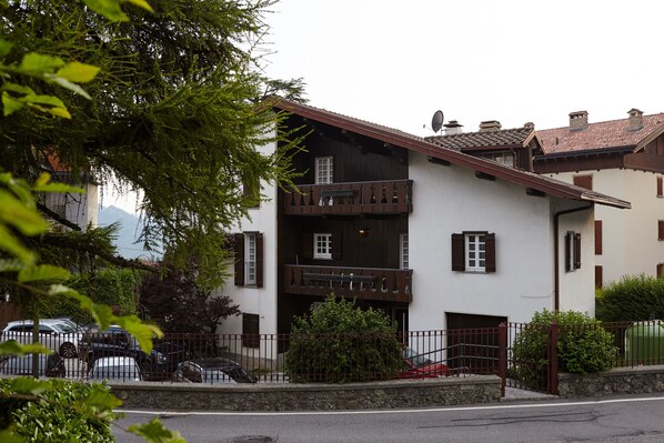 A two-story building with a balcony, a stone wall, and a metal fence. - Lo Chalet (Castione della Presolana)