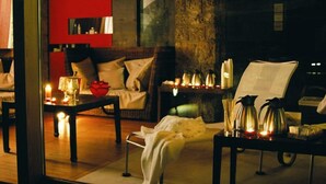 Une pièce chaleureuse avec un canapé, une table basse et un fauteuil. Il y a des bougies sur la table et une fleur rouge sur le canapé.