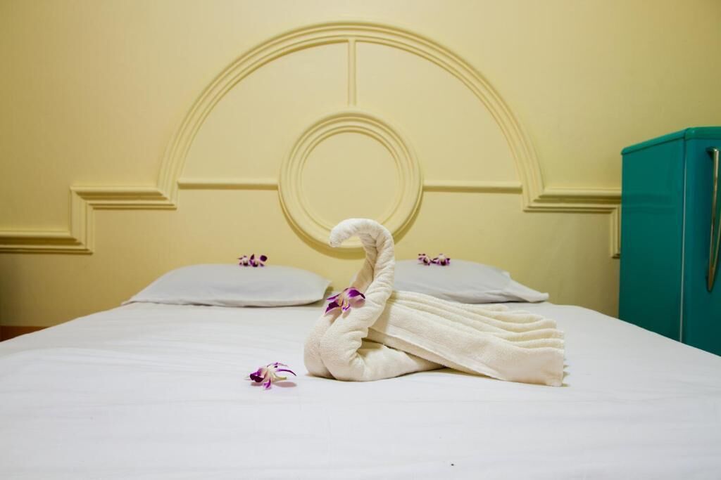 Ein ordentlich bezogenes Bett mit einem zu einem Schwan geformten Handtuch, Kissen und einem türkisblauen Schrank.