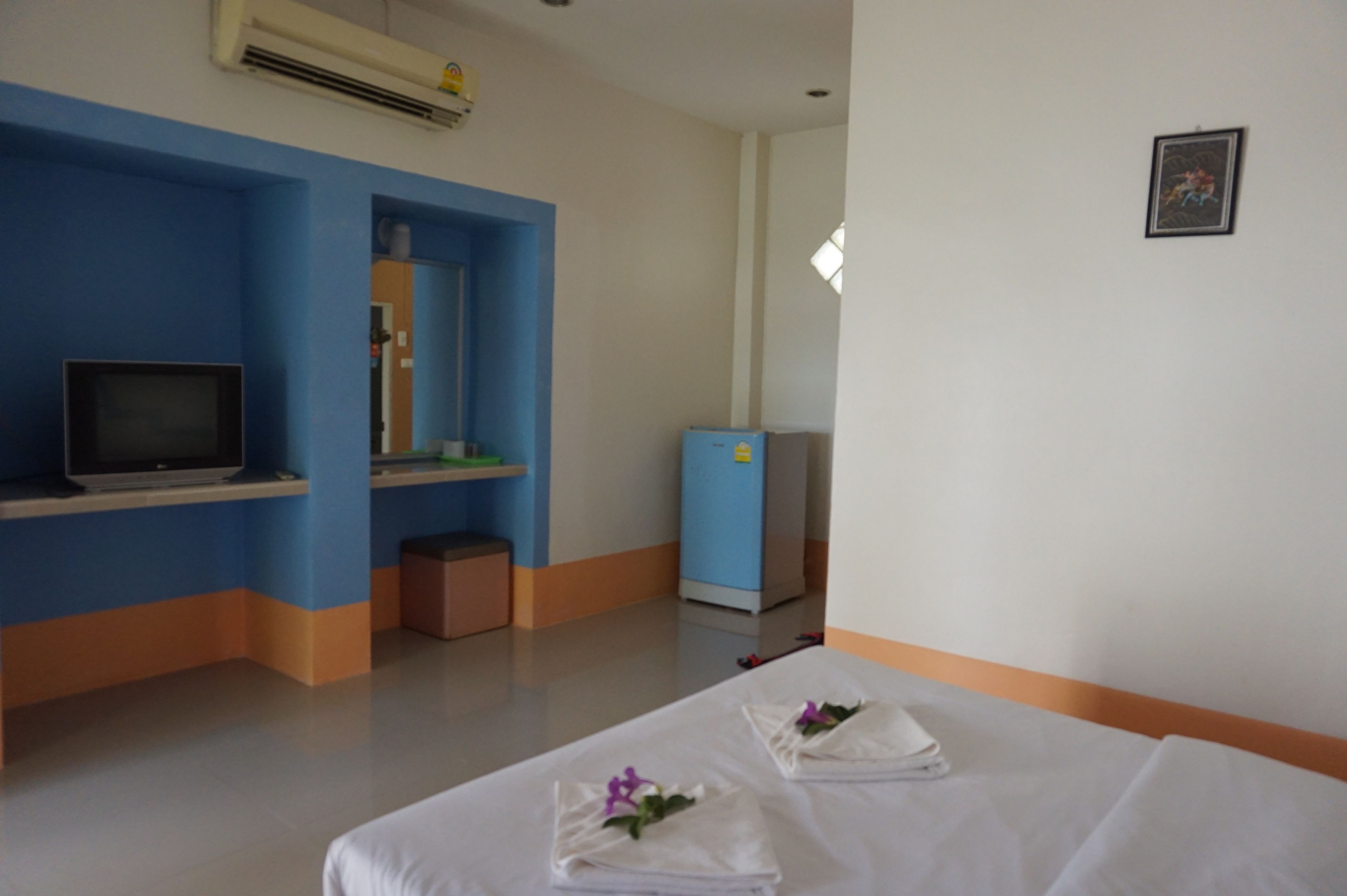 A hotel room with a bed, a television, a desk, and a blue refrigerator.
