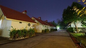 A row of single-story houses with red roofs and white walls, a paved driveway, and a well-lit street at night. - Ratchapreuk Resort (Kalasin)