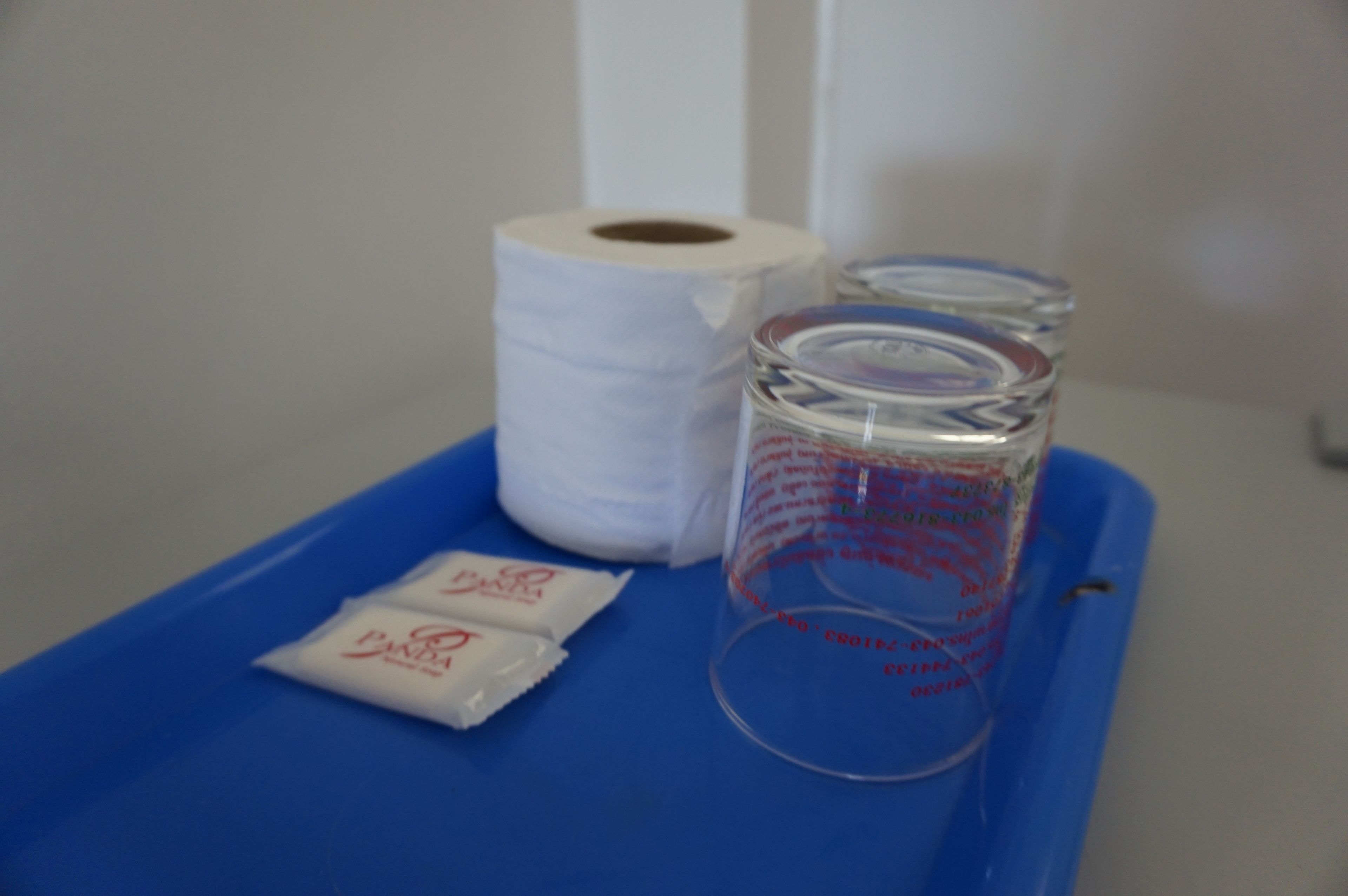 Una bandeja azul con un rollo de papel higiénico, una taza medidora y dos pequeños sobres.