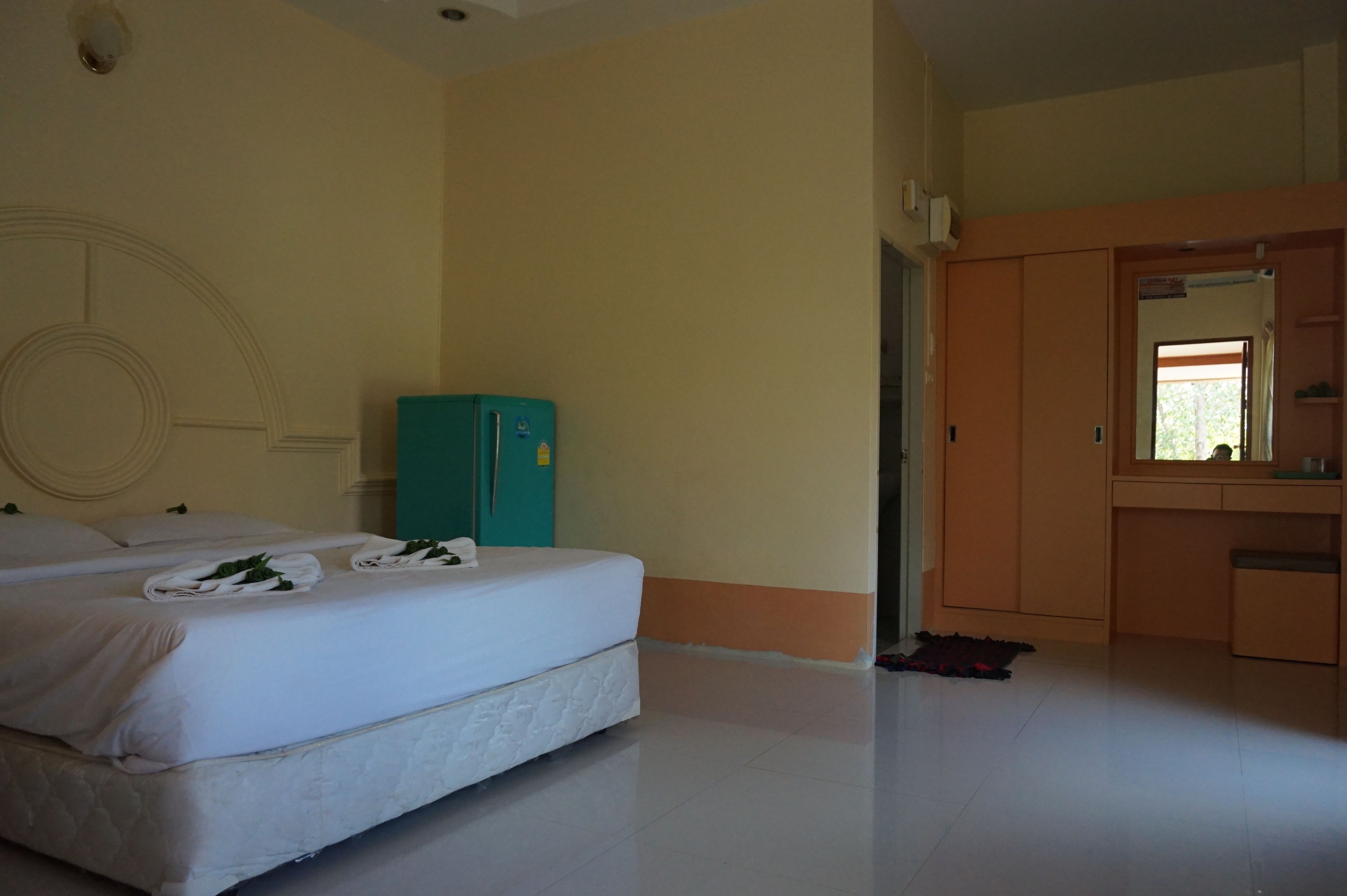 A hotel room with a bed, a small teal refrigerator, a wardrobe, and a mirror.