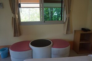 A room with a window, a round table with a black center, and a wooden shelf.