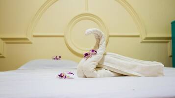 A neatly made bed with a towel shaped like a swan and a single purple orchid petal on the pillow.