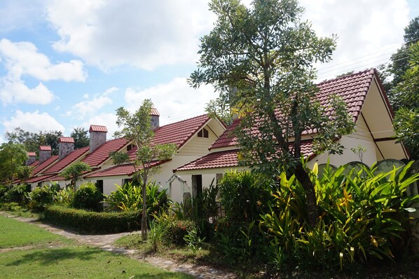 A row of white buildings with red roofs, surrounded by lush greenery and a clear sky.