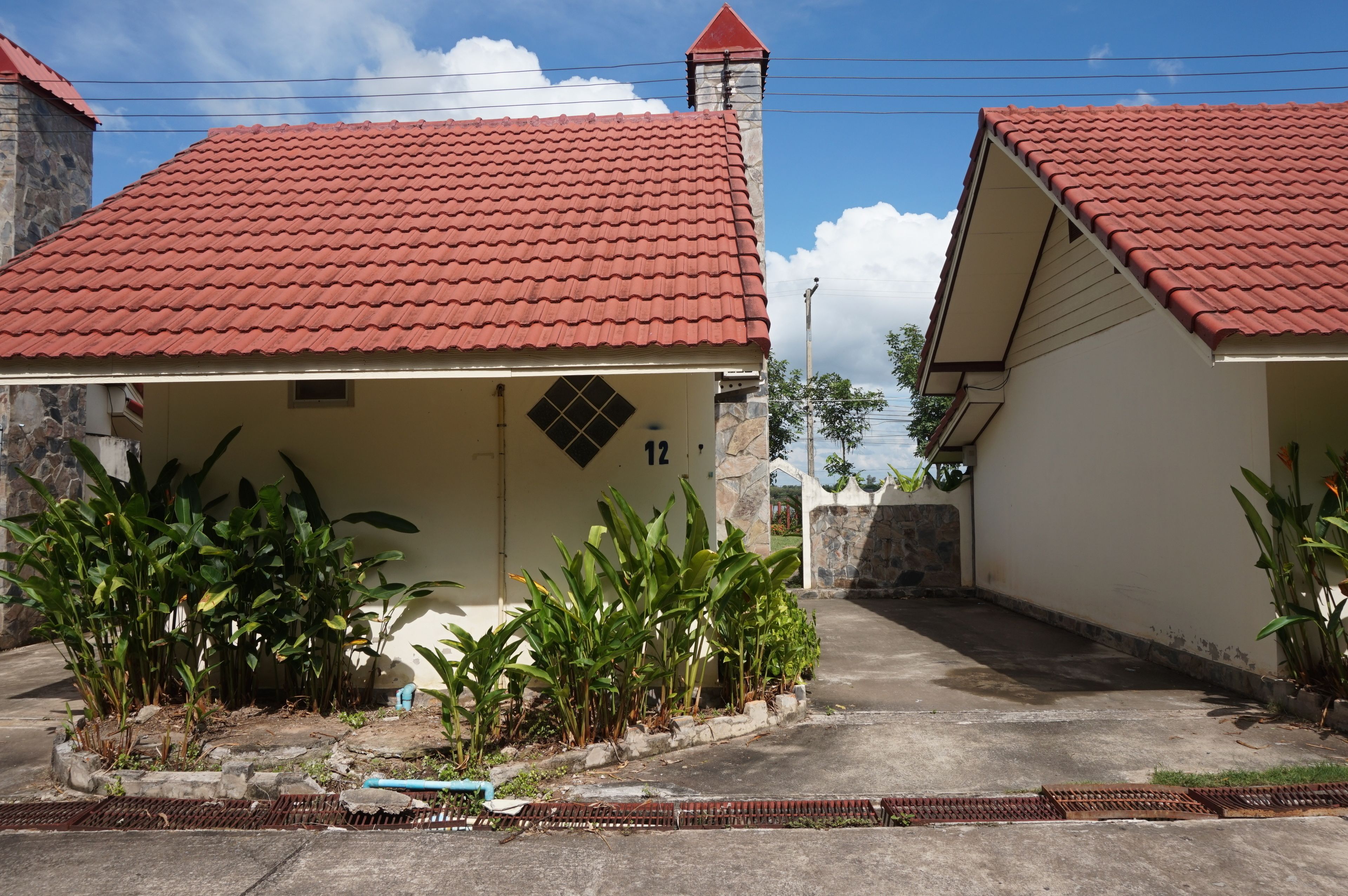 Two single-story buildings with red-tiled roofs, surrounded by lush greenery.