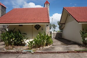 Two single-story buildings with red-tiled roofs, surrounded by lush greenery.