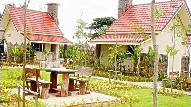 A bungalow-style hotel with a red-tiled roof, a central courtyard with a wooden table and benches, and lush greenery surrounding the property. - Ratchapreuk Resort (Kalasin)