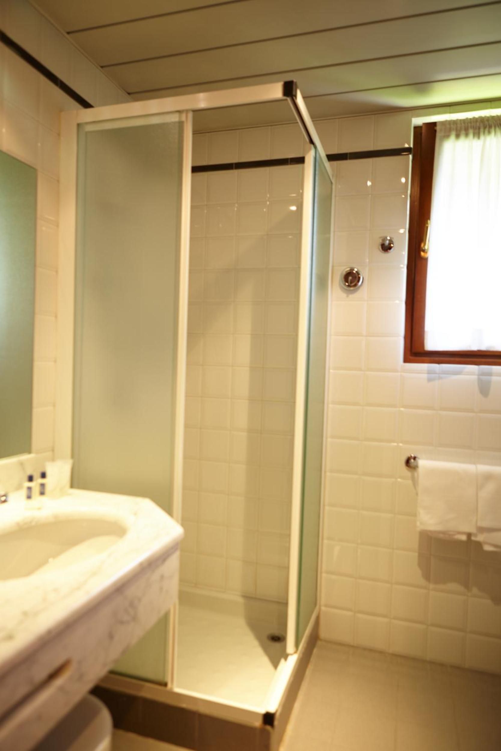 A bathroom with a glass-enclosed shower, a sink with a marble countertop, and a window with a curtain.