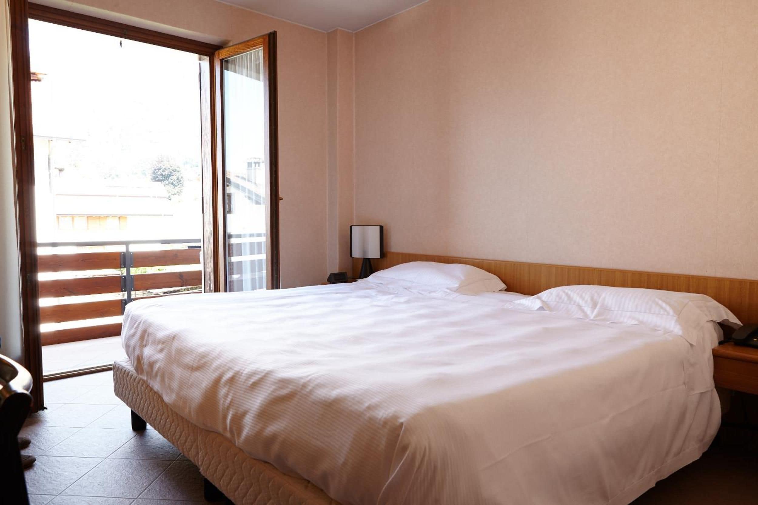 Une chambre d’hôtel comprenant un lit, une table de chevet, une lampe et une porte-fenêtre coulissante donnant sur un espace extérieur.