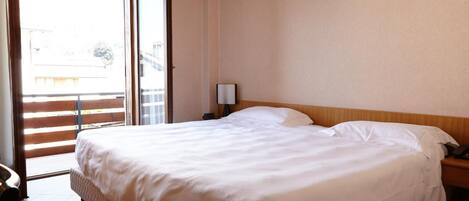 Une chambre d’hôtel comprenant un lit, une table de chevet, une lampe et une porte-fenêtre coulissante donnant sur un espace extérieur.