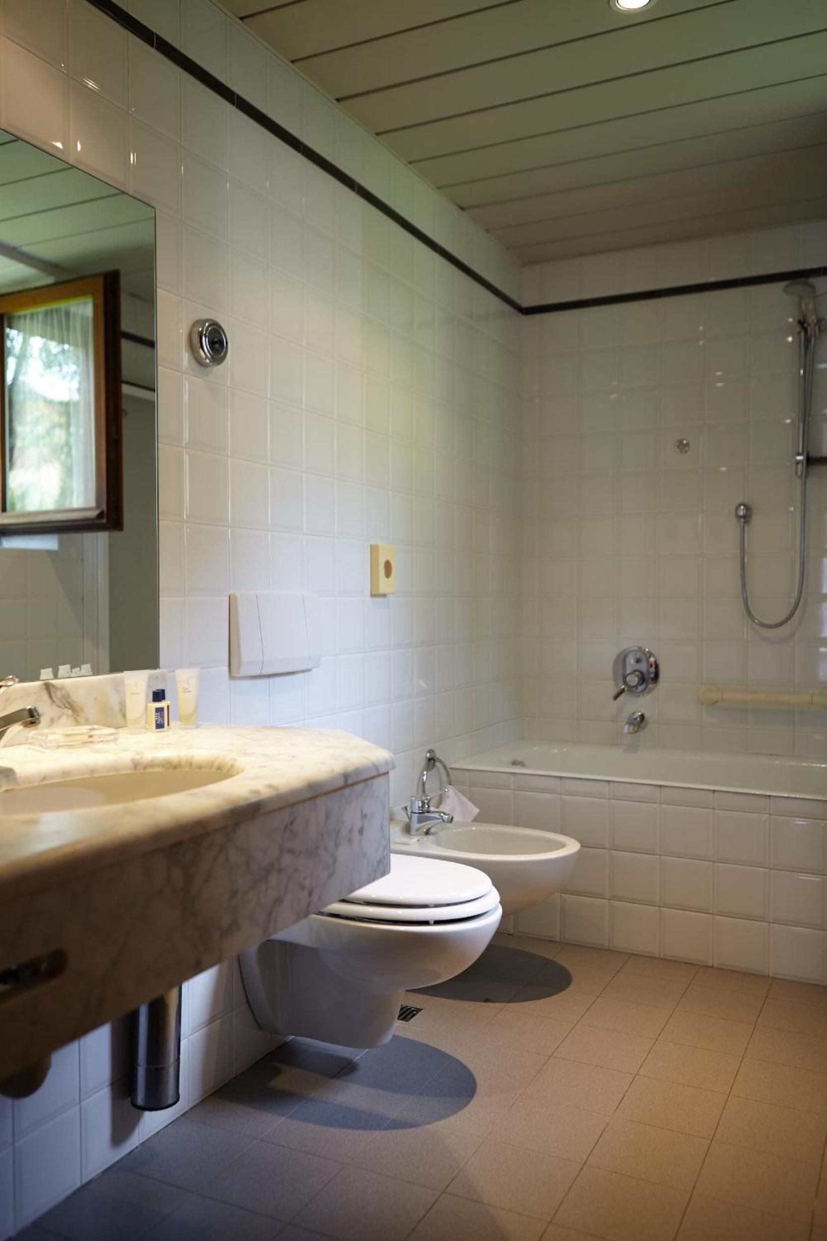 Et moderne badeværelse med en marmorvask, toilet, bidet og et badekar med brusehoved.