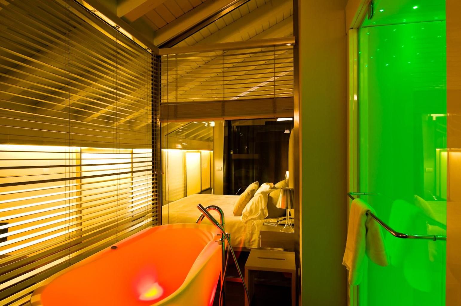 Een moderne badkamer met een badkuip, een spiegel en een muur verlicht in groen.
