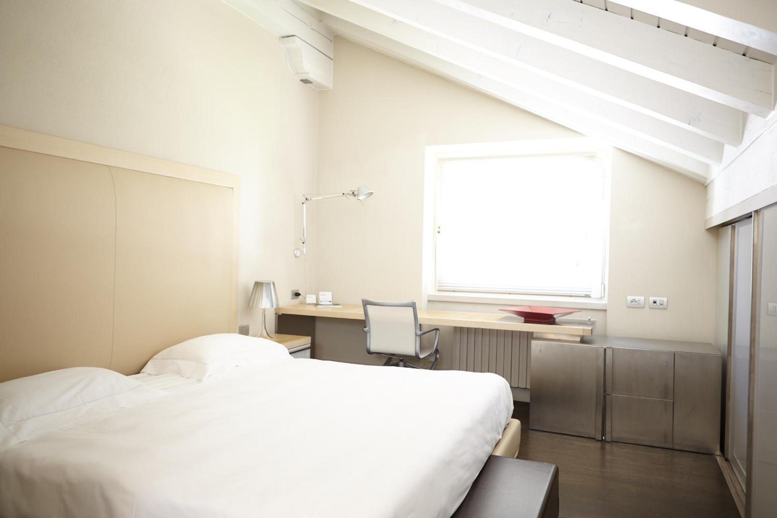 Habitación de hotel moderna con cama, escritorio, silla y ventana que proporciona luz natural.