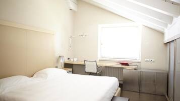 Habitación de hotel moderna con cama, escritorio, silla y ventana que proporciona luz natural.
