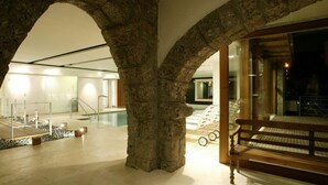 Un arc en pierre mène à un espace intérieur moderne comprenant une piscine, un banc en bois et une vue sur la piscine.