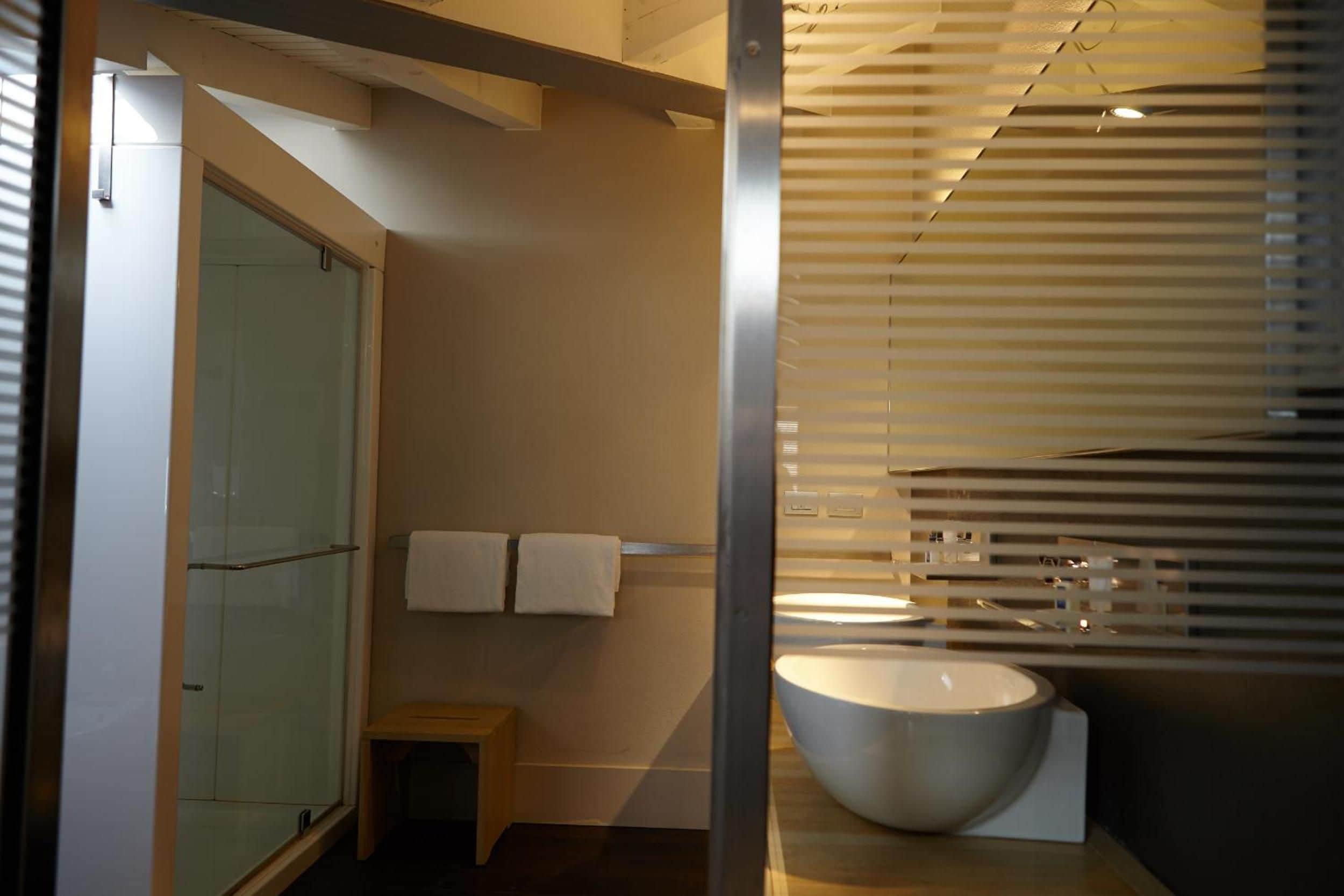 A modern bathroom with a large bathtub, a glass shower enclosure, and a small wooden stool.