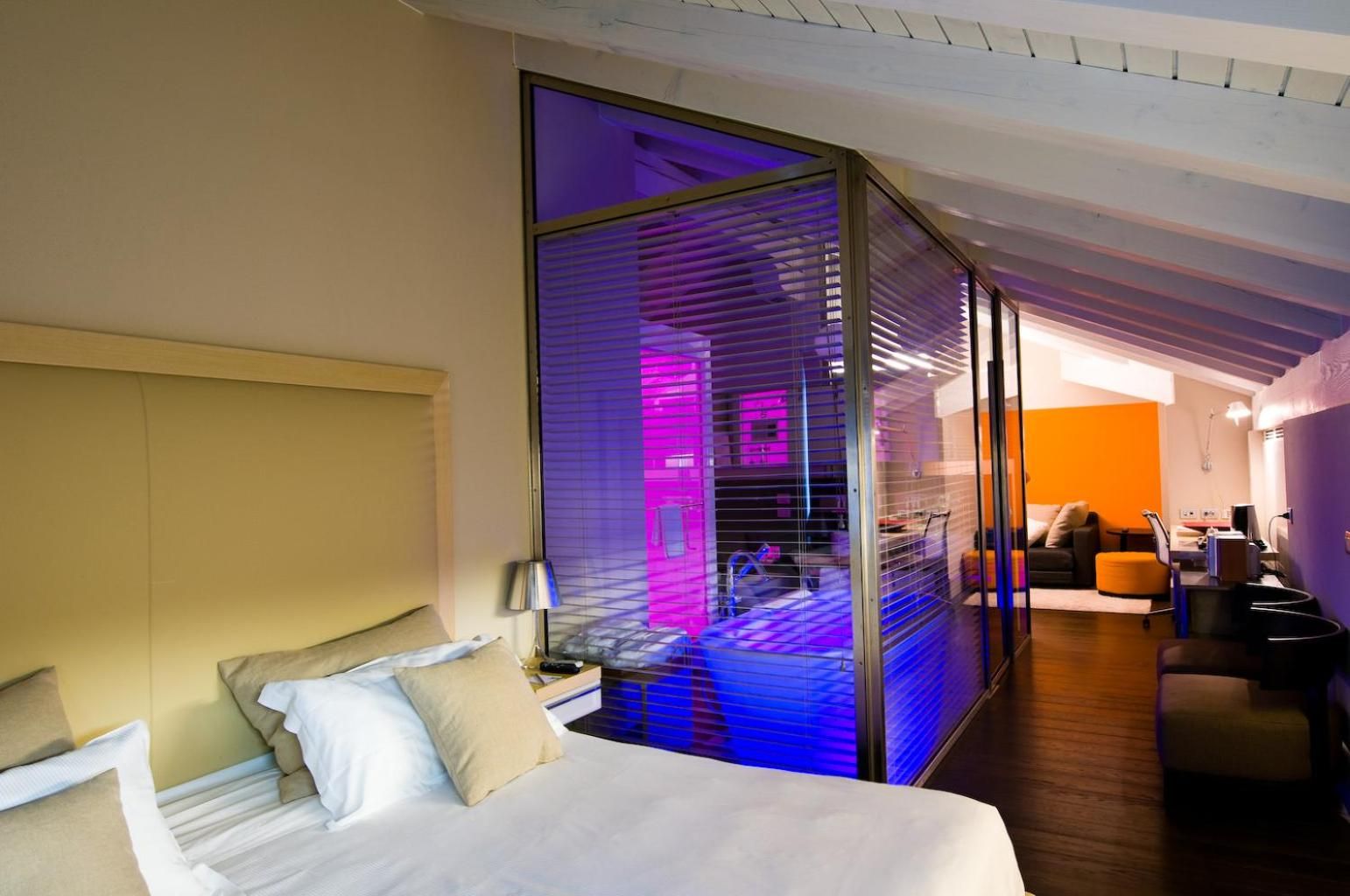 Une chambre d’hôtel moderne avec un grand lit, une cloison en verre et une vue sur l’espace de vie.