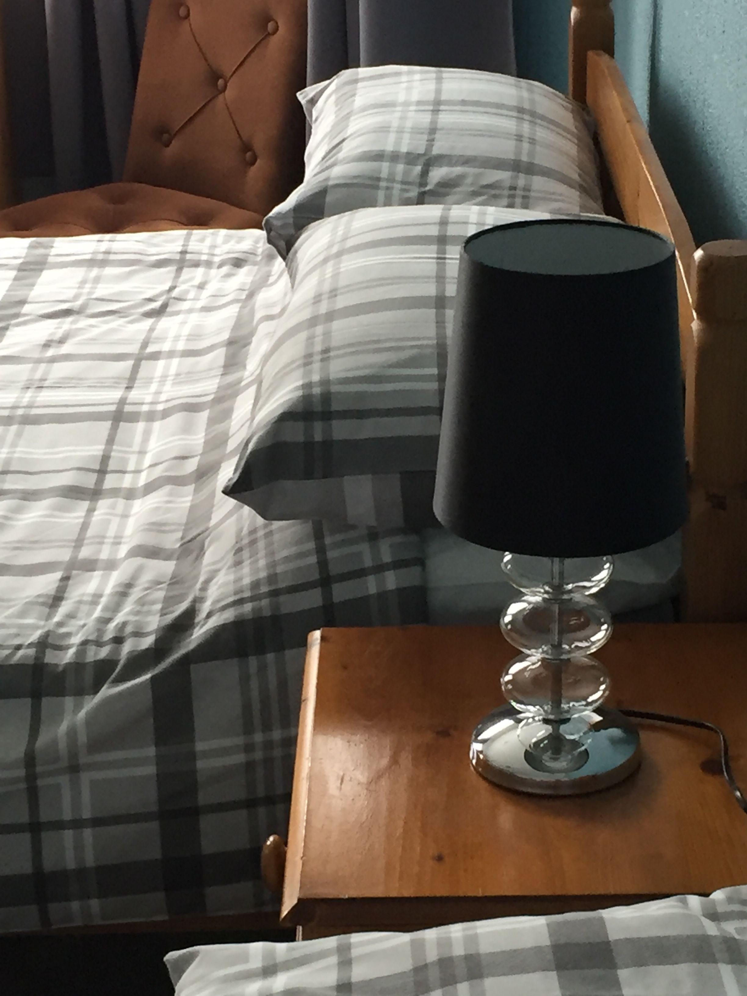 Una cama con ropa de cama escocesa, un cabecero de madera y una mesita de noche con lámpara.