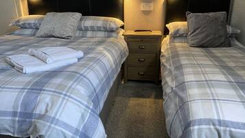 A hotel room with two beds, each with a grey and white checkered duvet, a small bedside table with a lamp, and a headboard with a textured design.