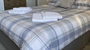 Uma cama bem arrumada com colcha xadrez, cabeceira e travesseiros.