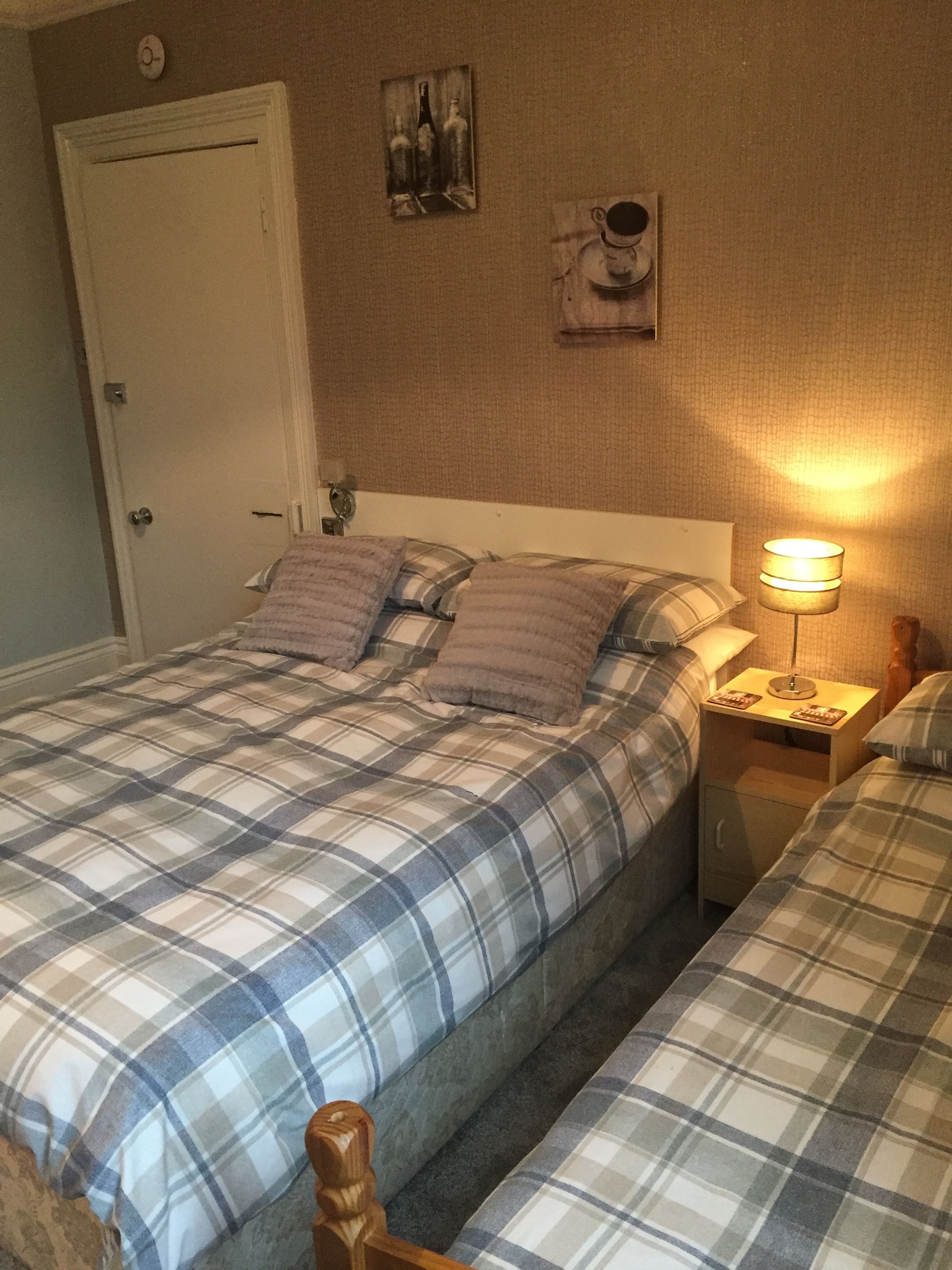 A bedroom with a double bed, a nightstand with a lamp, and a door.
