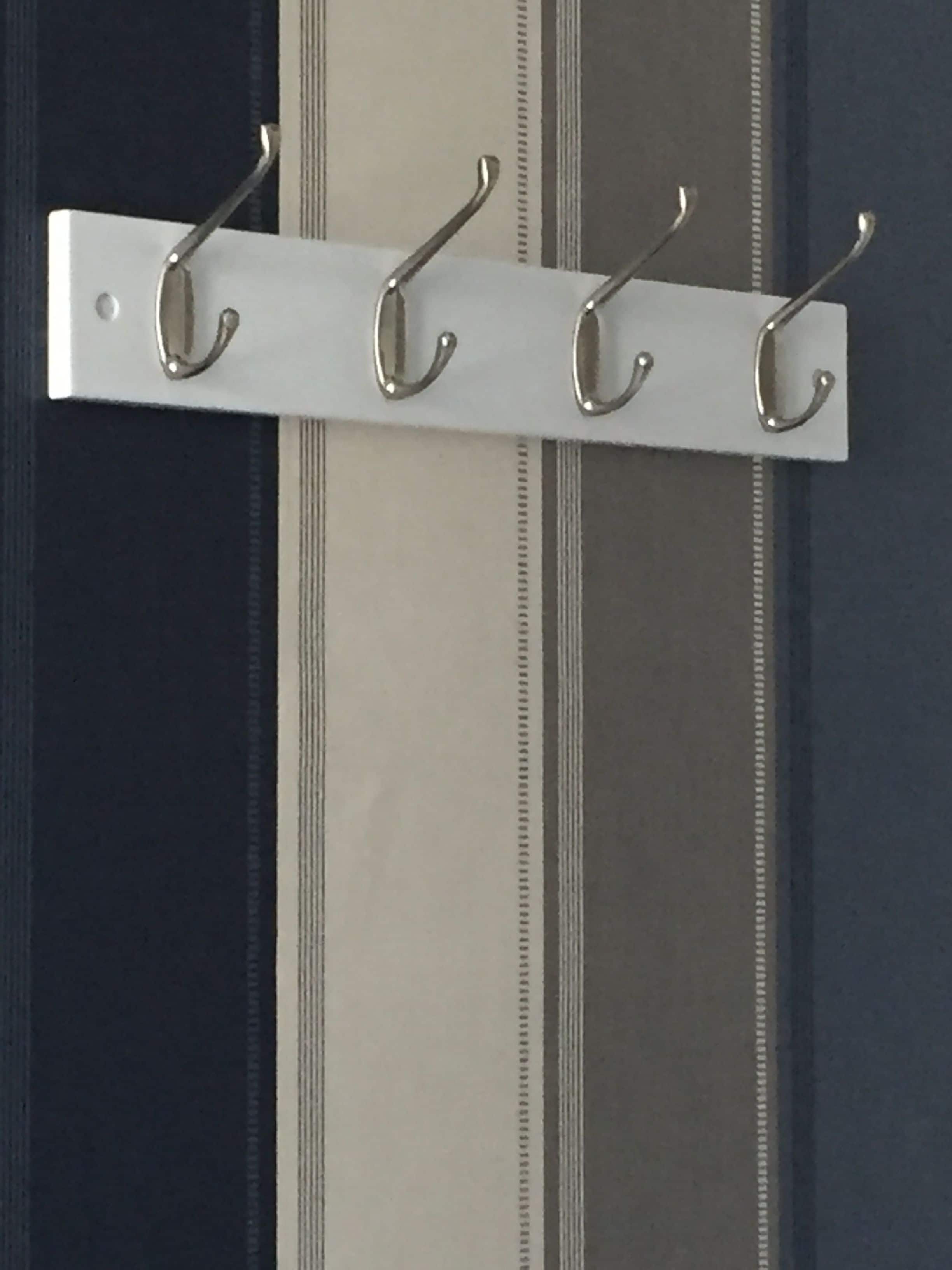 A metal coat rack with four hooks mounted on a wall.
