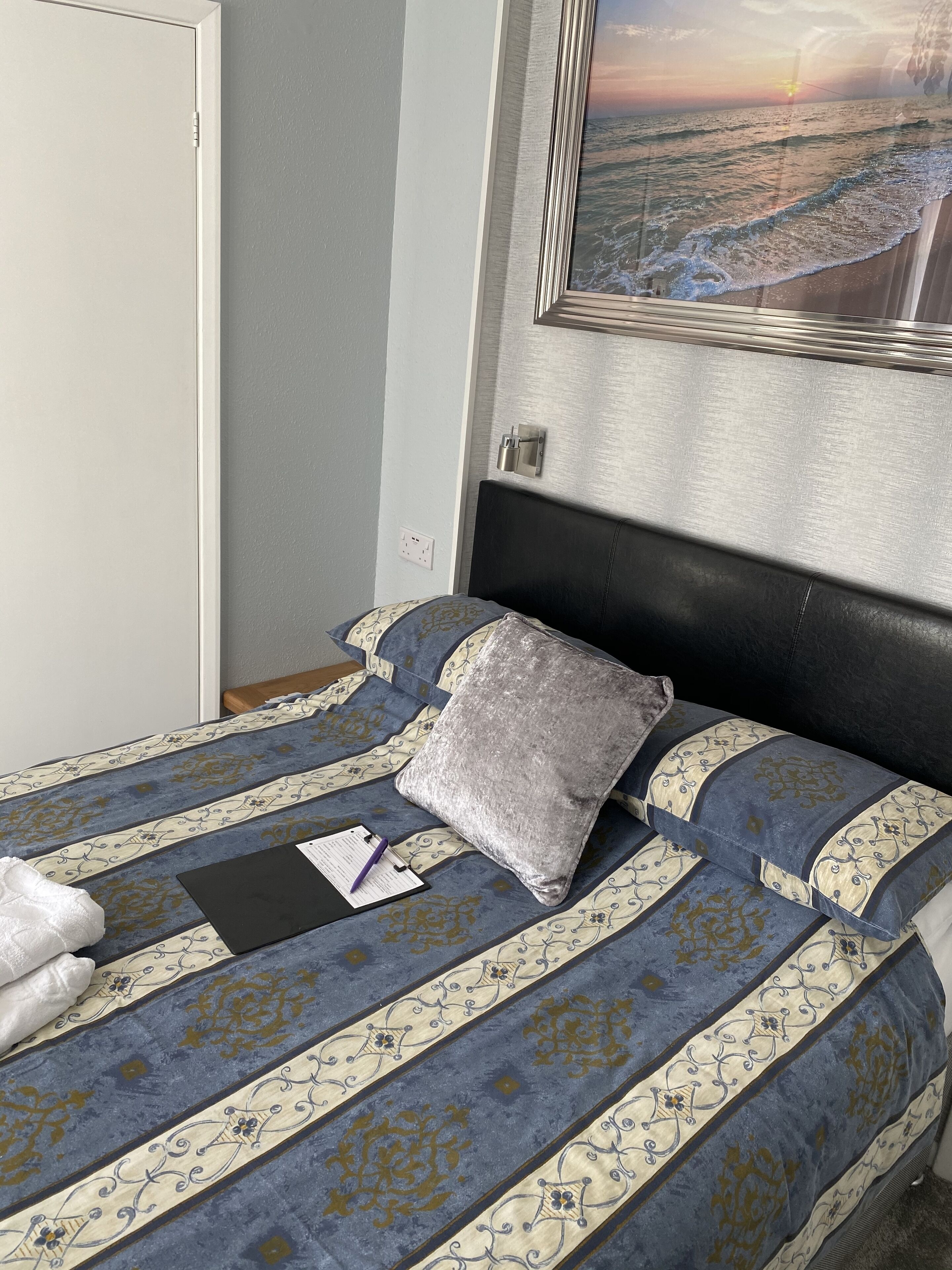A neatly made bed with a patterned bedspread, a pillow, and a folded towel.