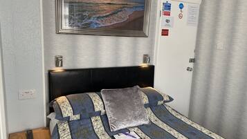 A neatly arranged hotel room with a bed, a nightstand, a remote control, a notebook, and a pen.