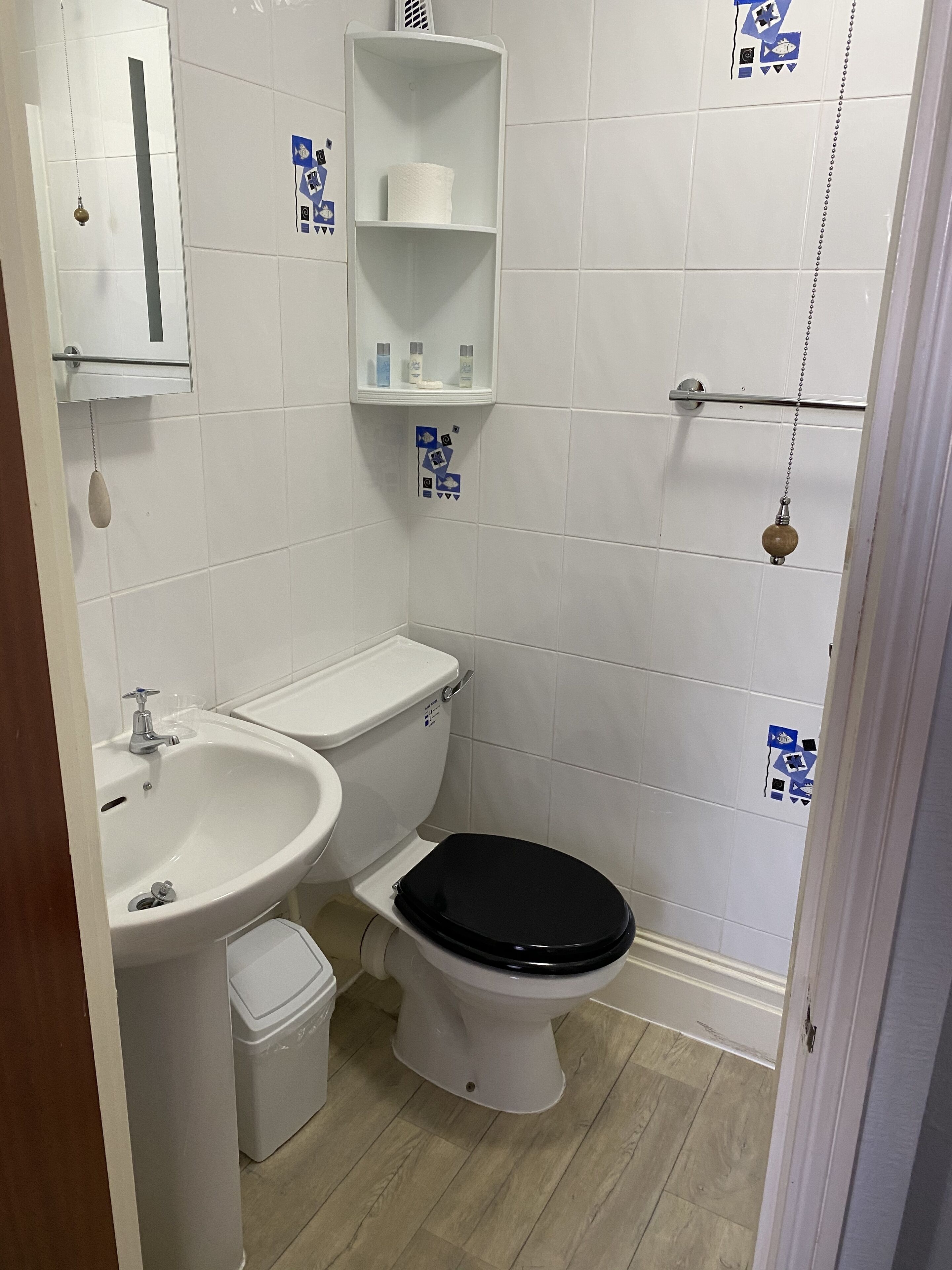 A small, clean bathroom with a toilet, sink, and shelves above the toilet.