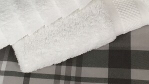 Uma cama com colcha xadrez e toalhas brancas dobradas.