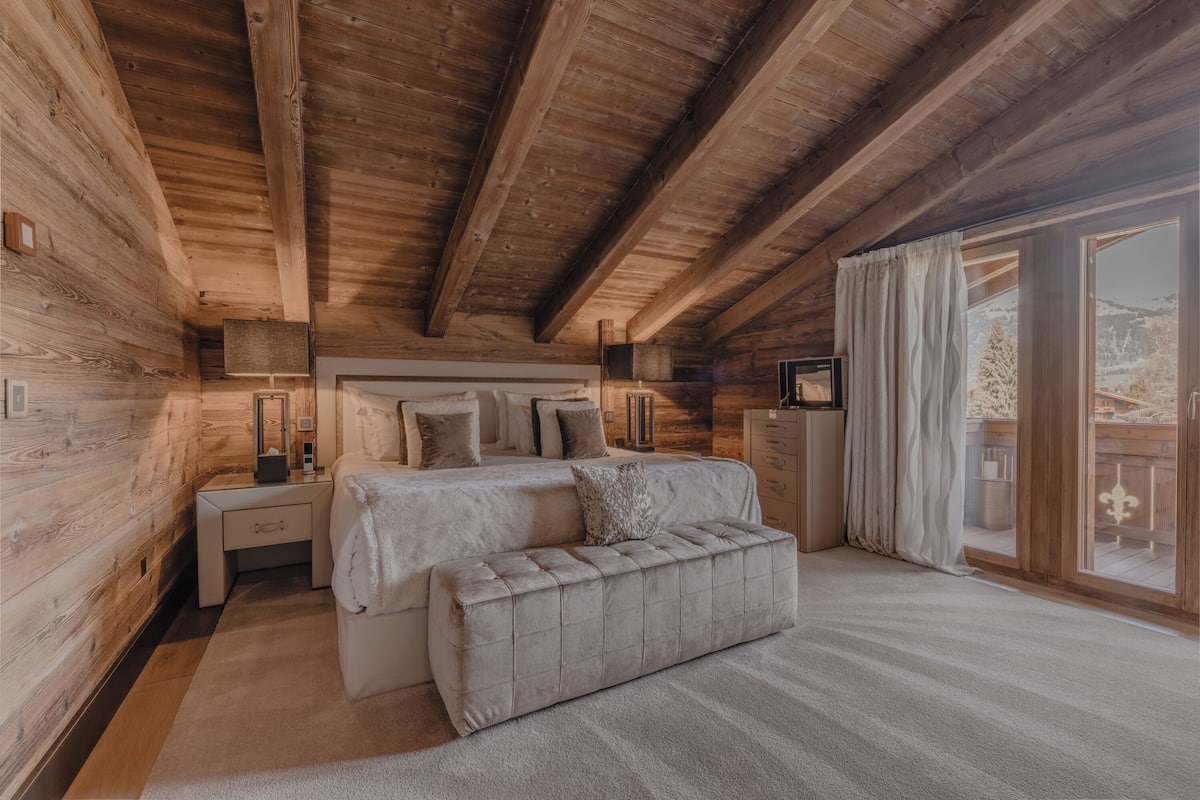 A log cabin bedroom with a bed, bedside tables, and a large window.