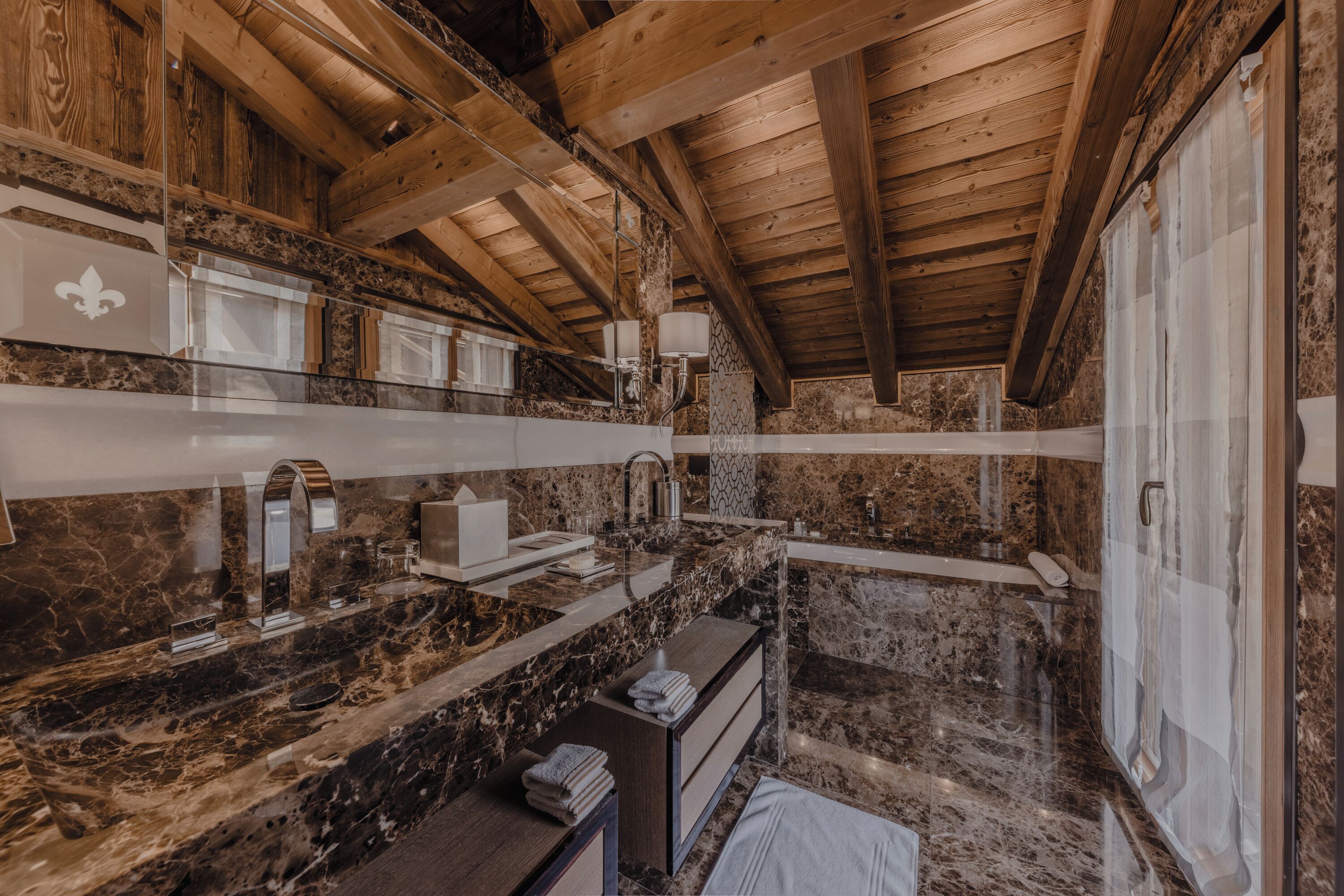 A rustic bathroom with marble countertops, wooden beams, and a large mirror.
