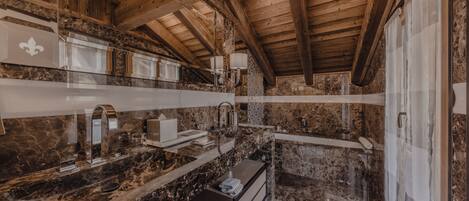 A rustic bathroom with marble countertops, wooden beams, and a large mirror.