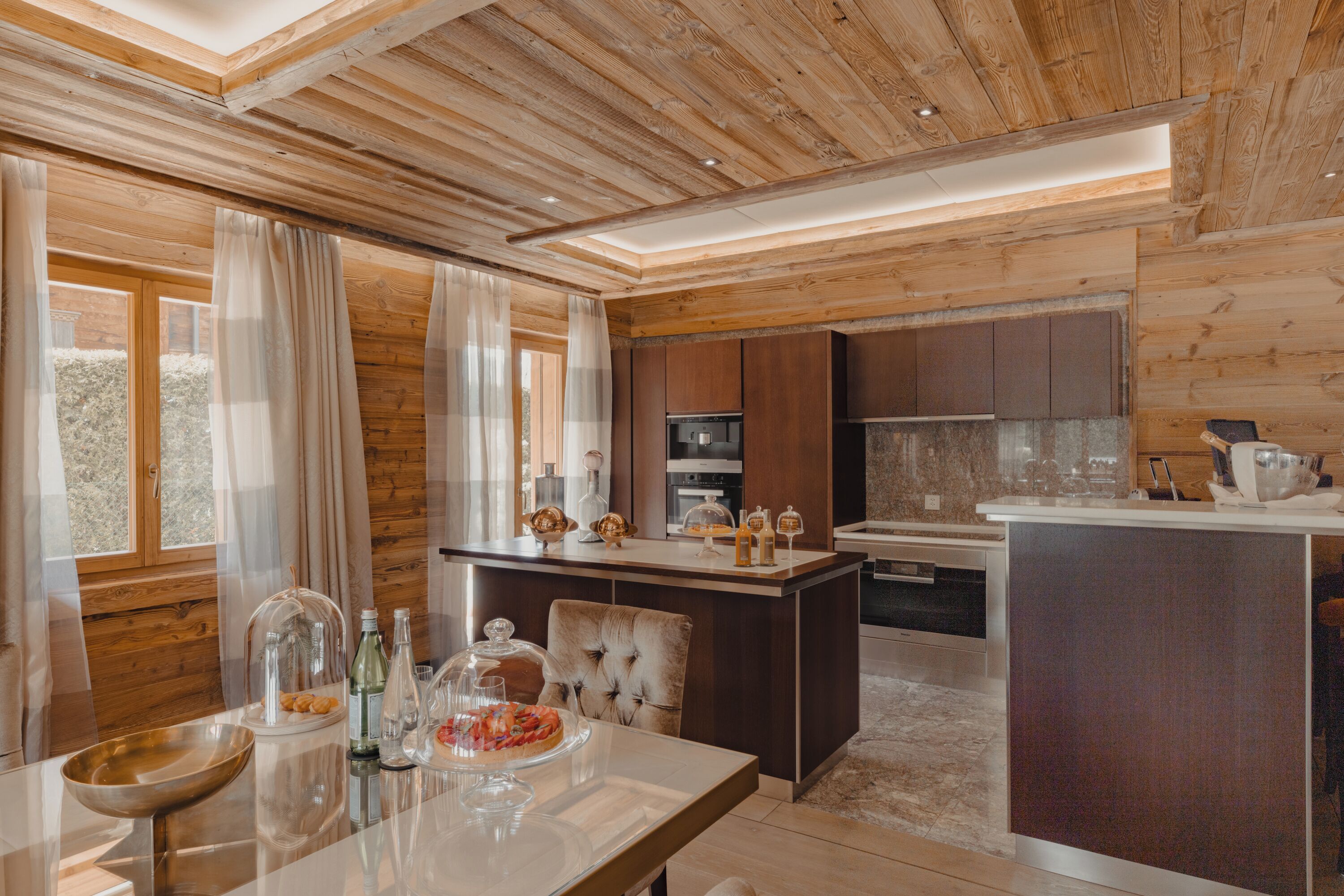 Une cuisine moderne avec un lambris en bois, un îlot central et un coin repas doté d’une table en verre.