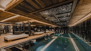 Een moderne spa met een groot binnenzwembad, houten balken in het plafond en een glazen scheidingswand.