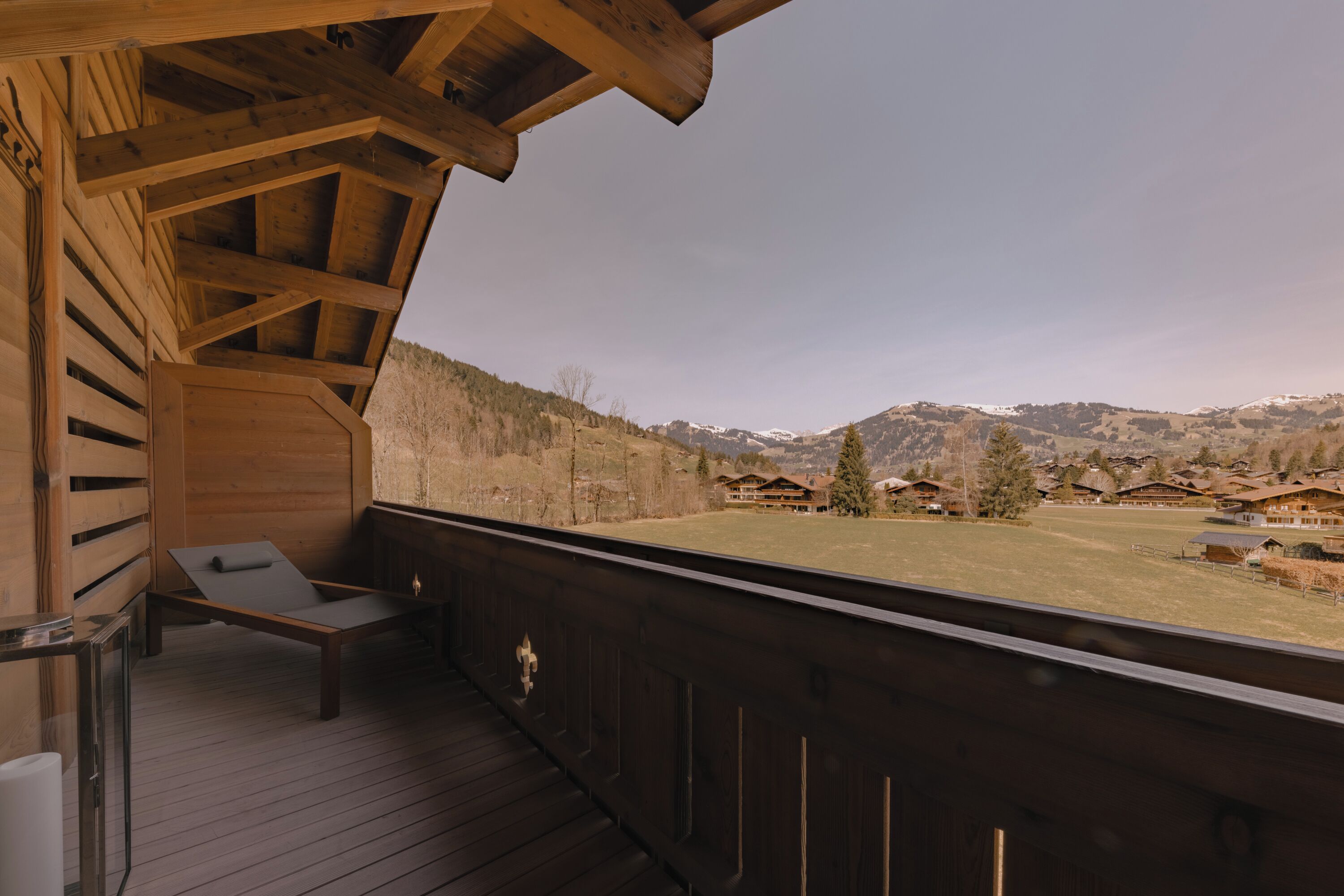 A wooden balcony with a view of a mountainous landscape and several houses.