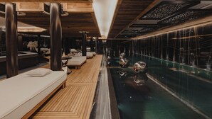 Een moderne spa-ruimte met houten vloeren, een zwembad met drijstoelen, en een zithoek met een massagetafel.