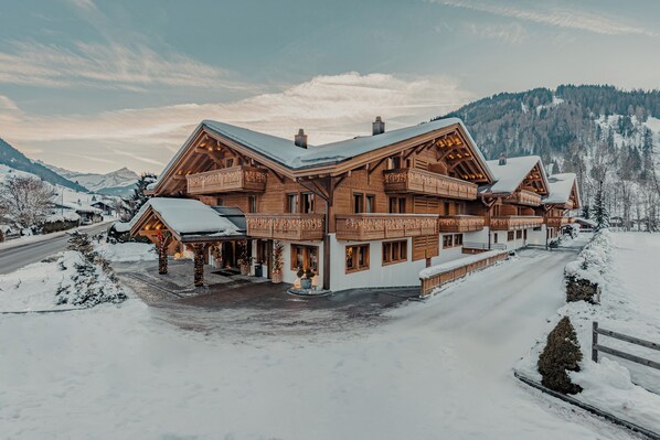 A large wooden chalet with multiple balconies and a snow-covered landscape. - Ultima Hotel Gstaad (Saanen)