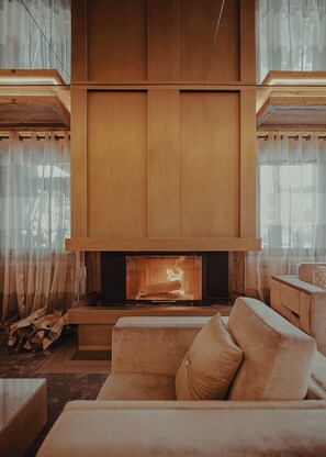 Una sala de estar moderna con una chimenea grande, paneles de madera y un sofá color beige.
