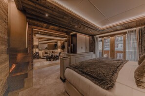 A modern bedroom with a large bed, a fireplace, a wooden ceiling, and a view of the outdoors. - Ultima Hotel Gstaad (Saanen)