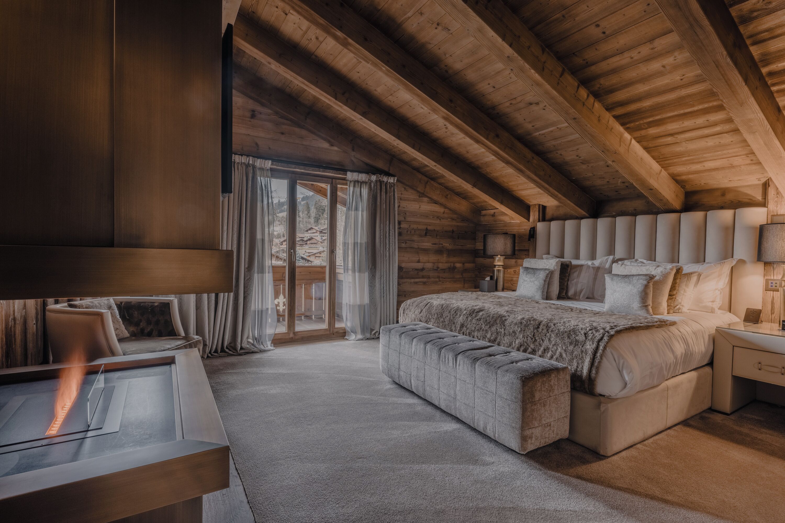 A cozy bedroom with a large bed, a bedside table, a lamp, and a view of the outdoors through a glass door.
