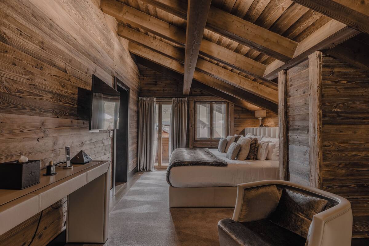 A cozy log cabin bedroom with a bed, a desk, and a chair.