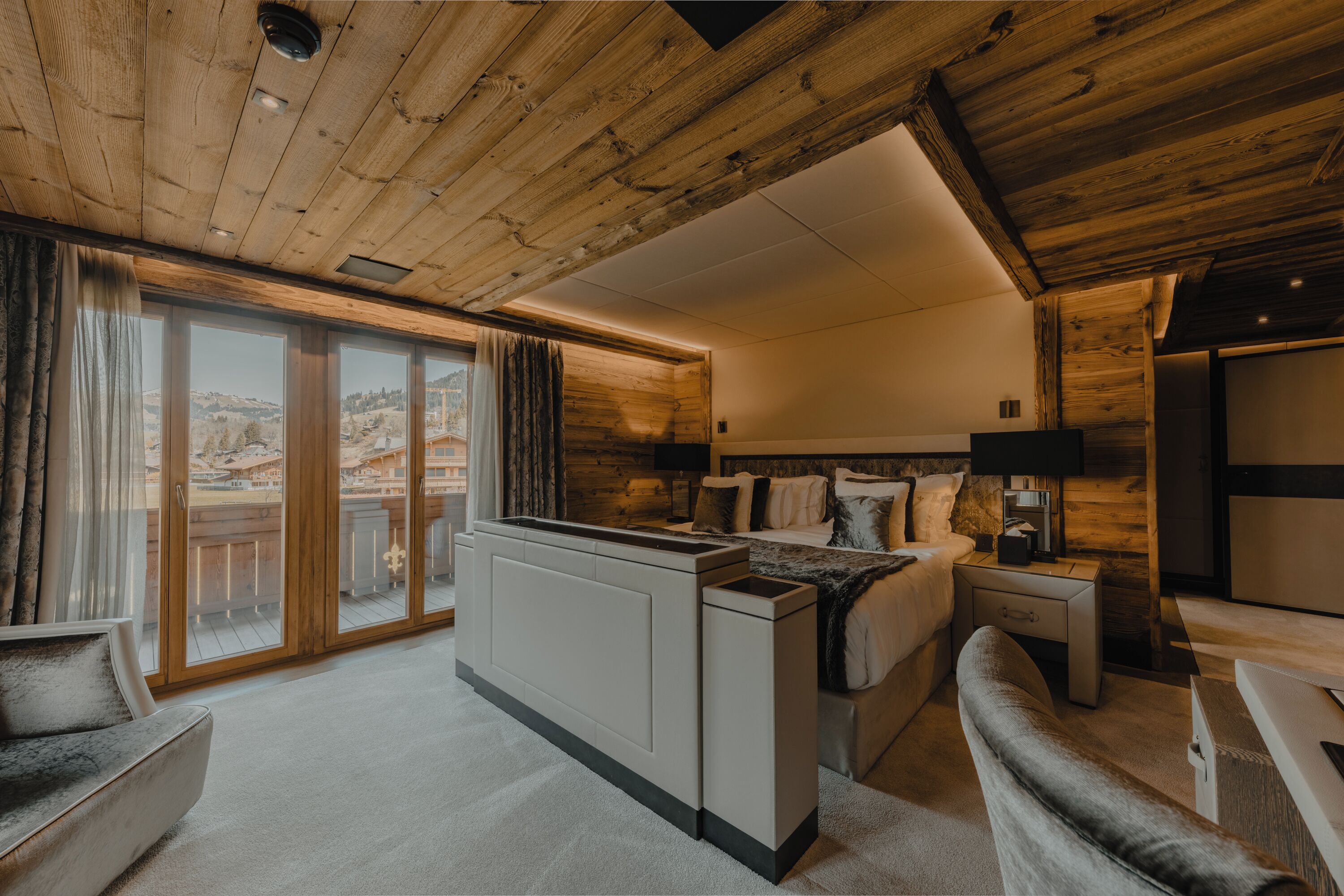 Un interno moderno con soffitto in legno, un'ampia porta scorrevole in vetro, un divano, un letto e un piccolo tavolino.