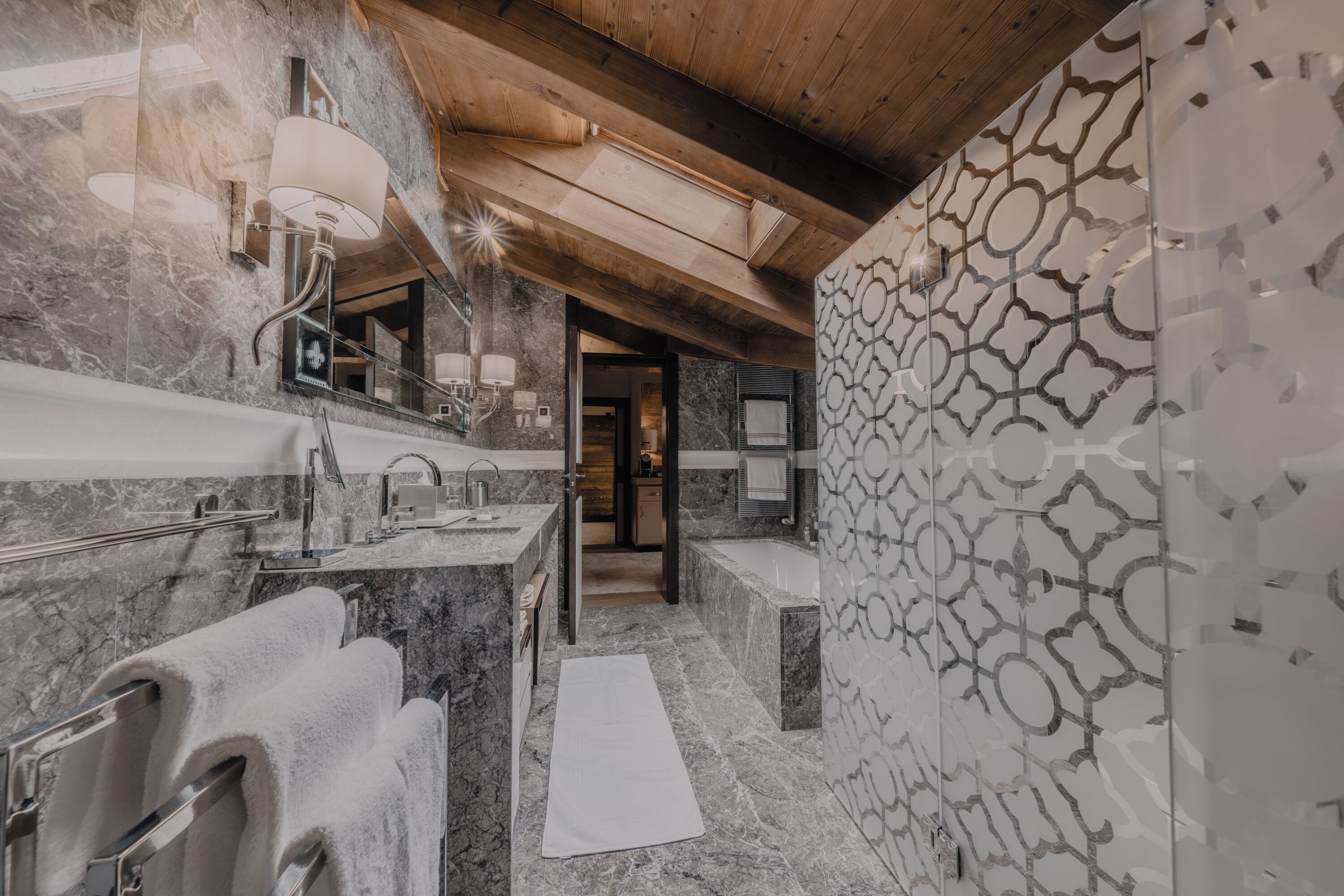 A modern bathroom with marble countertops, a large mirror, and a wooden ceiling.